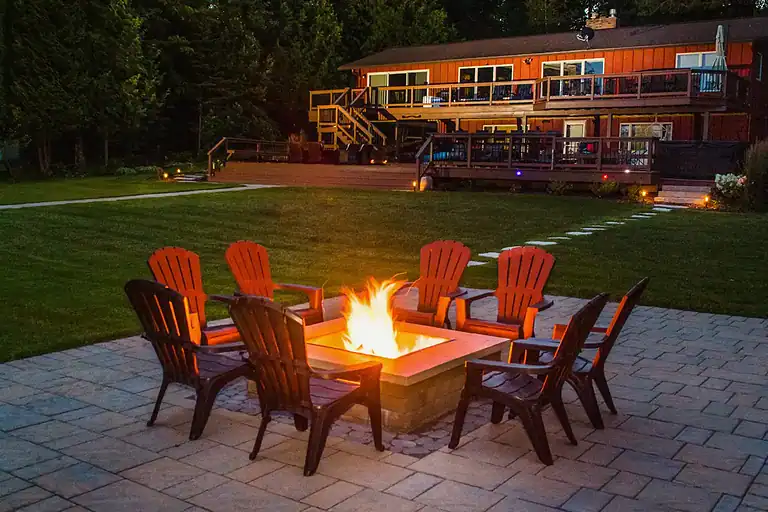 Gas fire pit ringed by seating on a paver patio at dusk by Miller Creek