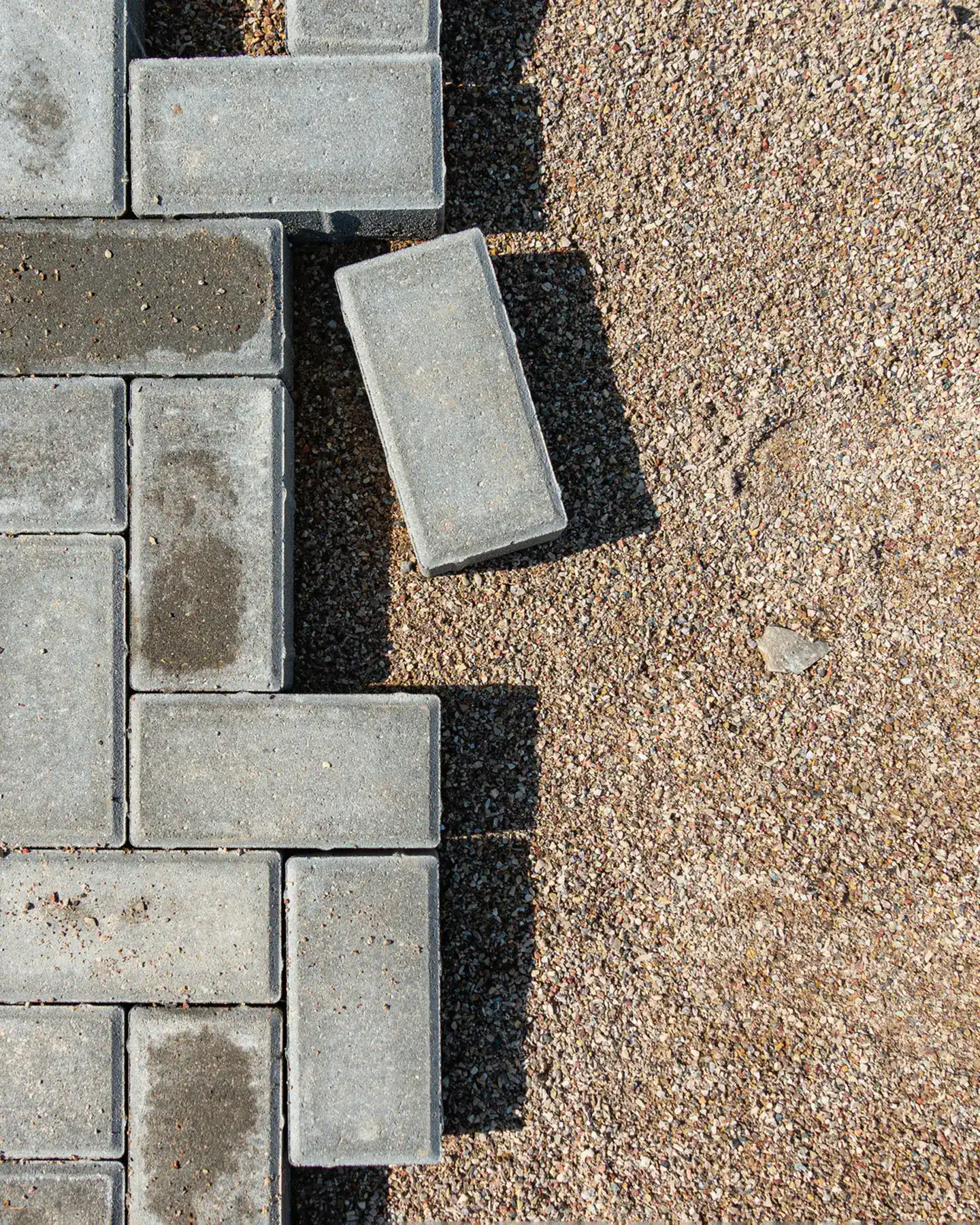 Paver walkway edge set against the compacted bedding base, one paver still loose